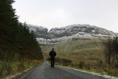 Rear view of man walking on road against mountains