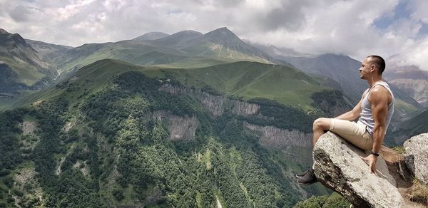 Man sitting on mountain against sky