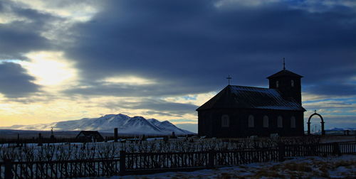 Church by snow covered field against cloudy sky