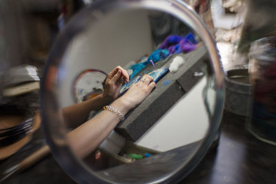 Cropped hands of female artist reflecting on mirror while making yarn art in workshop