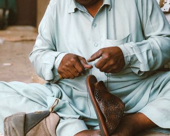 Midsection of man sewing sandal while sitting outdoors