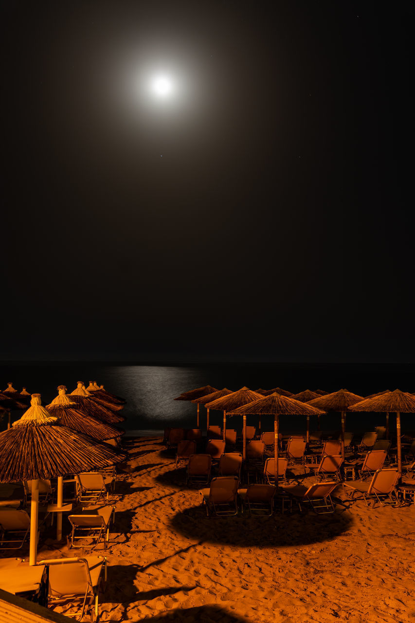 CHAIRS AND TABLE ON BEACH AGAINST SKY AT NIGHT