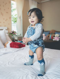 Cute baby girl standing on bed at home