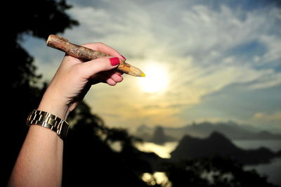 Cropped hand of woman holding wooden pencil against sky