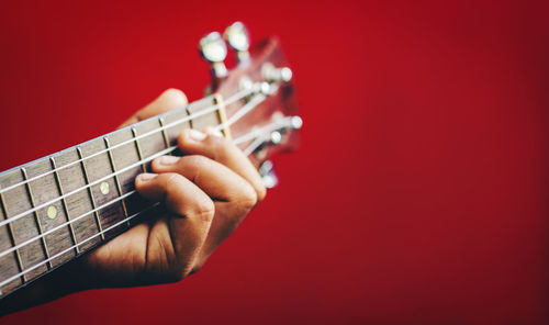 Close-up of hand playing guitar against red background