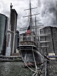 Sailboats in river by buildings against sky