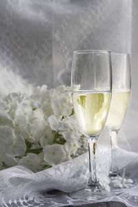 Two glasses of champagne on a background of white flowers for a romantic celebration