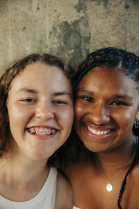 Happy teenage girl wearing braces by female friend against wall