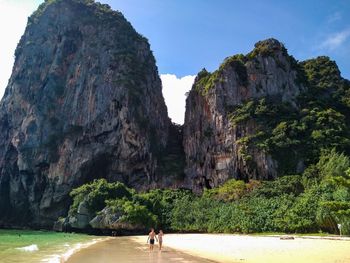 Couple walking on beach against rock formations