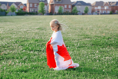 Little girl toddler wrapped in large canadian flag walking in park meadow outdoor. canada day 