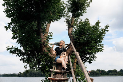 Side view of woman sitting on slide while standing by lake