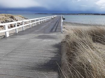 Footpath leading towards sea against sky