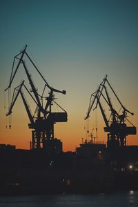 Silhouette cranes at commercial dock against sky during sunset