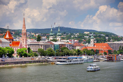 View of buildings by river against cloudy sky in city