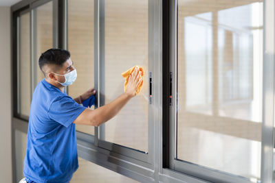 Man holding glass while standing by window