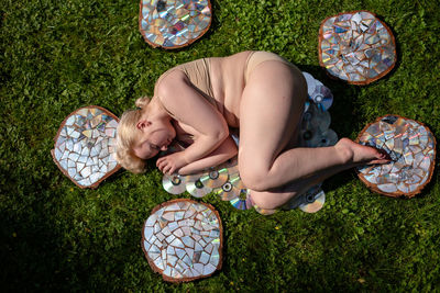 Top view of a young woman lying on a lawn among reflective wooden stumps