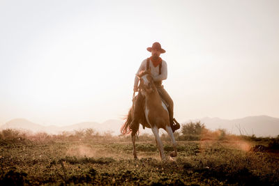 Silhouette cowboy riding a horse carrying a gun under beautiful sunset