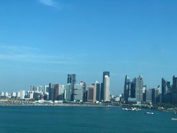 Sea by modern buildings against blue sky