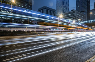 Light trails on city street by illuminated buildings at night