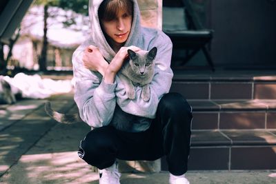 Boy with cat crouching on footpath