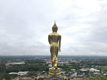 Statue of buildings in city against cloudy sky