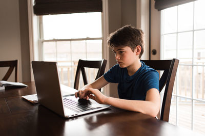 Tween boy working on his homework on a laptop commuter at home.