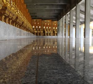 Golden buddha statues reflection on marble flooring at temple