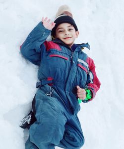 Portrait of smiling boy lying on snow covered land