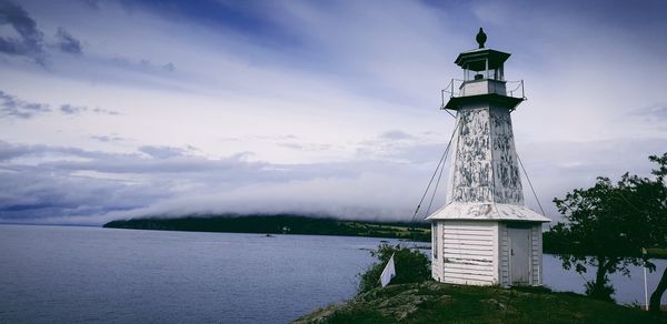 Lighthouse by building against sky