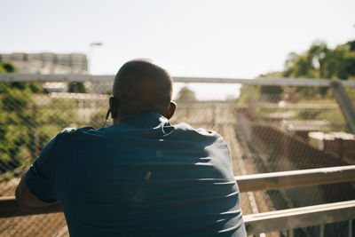 Rear view of exhausted male athlete leaning on railing during sunny day