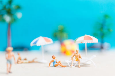 Miniature people wearing swimsuit relaxing on the beach with blue background