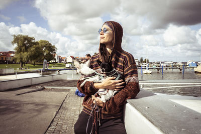 Strong woman in sun glasses by boats holds two dogs in sunlight