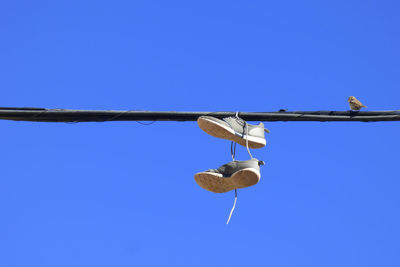 Low angle view of shoes hanging on cables against clear blue sky