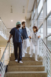 Low angle view of senior female doctor discussing with colleagues while moving down on steps in hospital