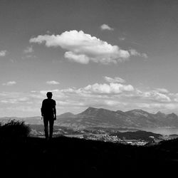 Rear view of man watching mountains against sky