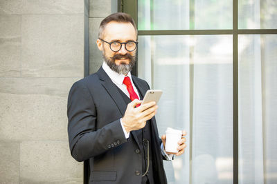 Smiling businessman using smart phone while sitting outdoors