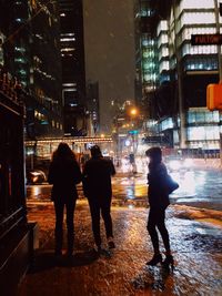 Rear view of people walking on illuminated street at night