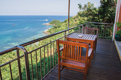 Empty chairs and table by sea against sky seen from balcony