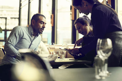 Male and female customers ordering to female owner while sitting in cafe