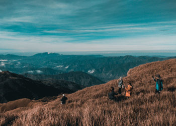 People photographing on field by mountains against cloudy sky