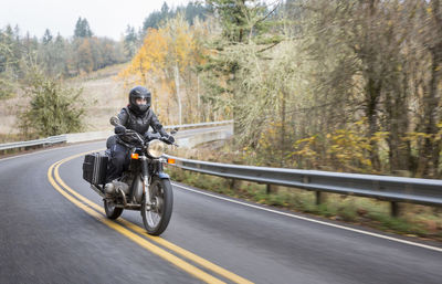 Female biker wearing crash helmet while riding motorcycle on country road