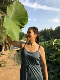 Woman holding leaf while standing by plants