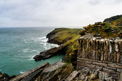 Scenic view of sea by cliff against cloudy sky