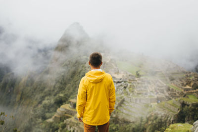 A man in a yellow jacket is standing near ruins of machu picchu, peru