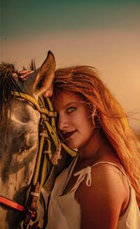 Portrait of young woman with horse against sky during sunset