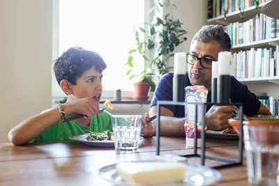 Father and son eating food while sitting at dining table