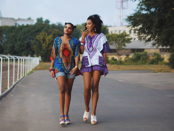 Young female friends walking at race course against sky