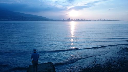 Rear view of man standing in sea against sky