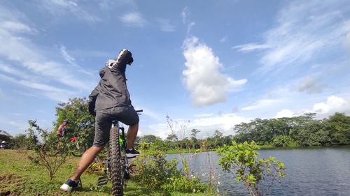 Man riding bicycle by lake against sky