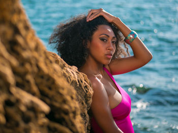 Portrait of beautiful young woman leaning on rock by sea